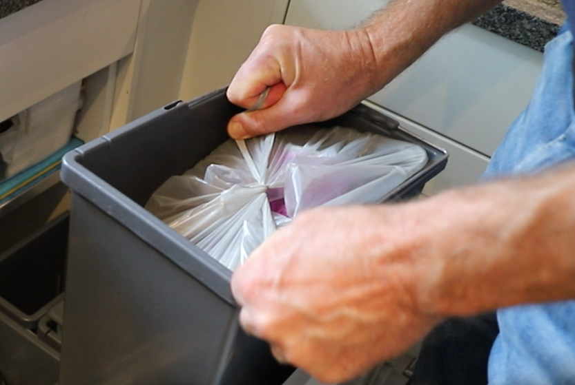 Två händer knyter ihop en plastpåse som innehåller plastförpackningar.