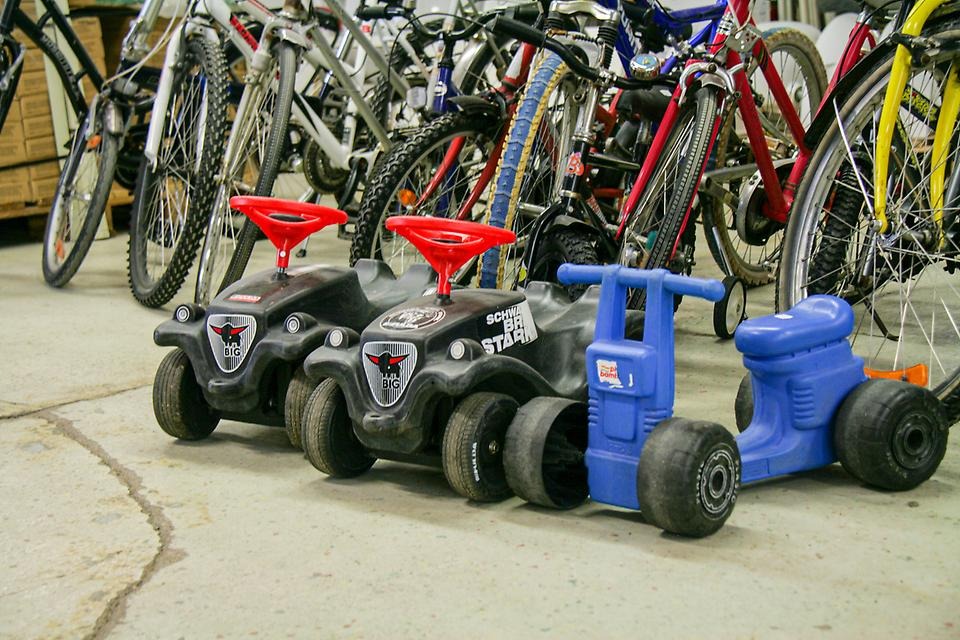 Två svarta och en blå bobby car står framför en rad med cyklar.