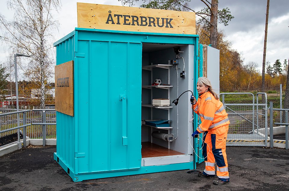 Bild: Kvinna i orange kläder bär i en lampa i en turkos container för återbruk